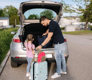 Pai com a filha a pôr malas de viagem no carro