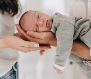 bebé a dormir nas mãos dos pais 
