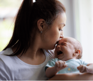 mãe a dar beijinho na testa de bebé a chorar