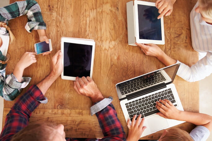 Uma família a utilizar dispositivos móveis à mesa