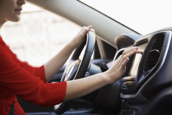 mulher ao volante a tocar no ecrã do tabliê