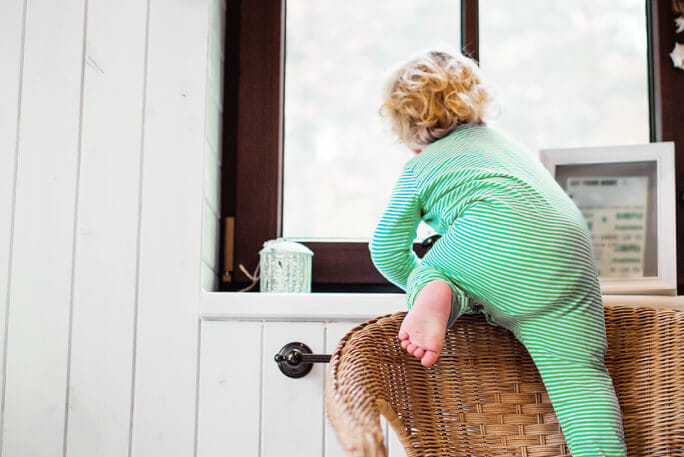 Criança pequena sobe de uma cadeira para uma prateleira, arriscando a segurança 