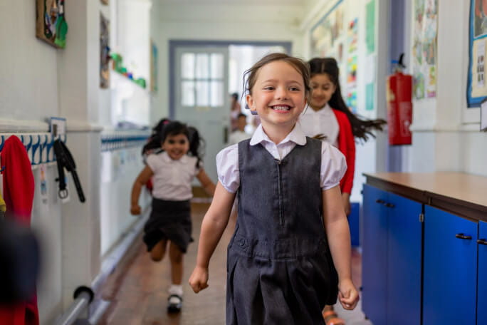 Três meninas felizes num corredor de escola.