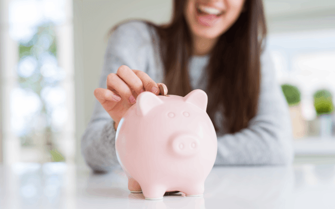 Jovem mulher feliz coloca uma moeda num porquinho-mealheiro.