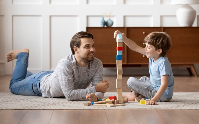 Pai brinca com filho pequeno fazendo torres de cubos.