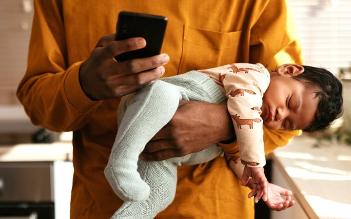 Pai a segurar um bebé adormecido enquanto utiliza o telemóvel.