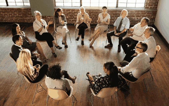 Várias pessoas num espaço interior sentadas em roda, conversam entre si.