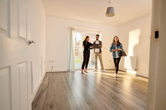 Um casal jovem, acompanhado de uma promotora imobiliária, visita uma casa à venda. 