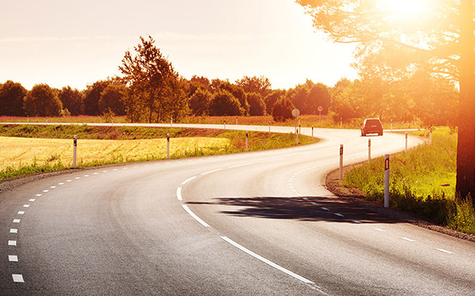 Imagem de estrada com carro ao fundo.