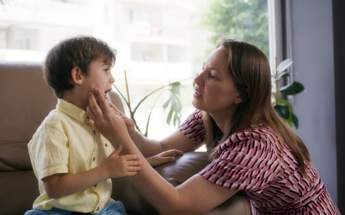 Mulher analisa uma afta no lábio de uma criança.