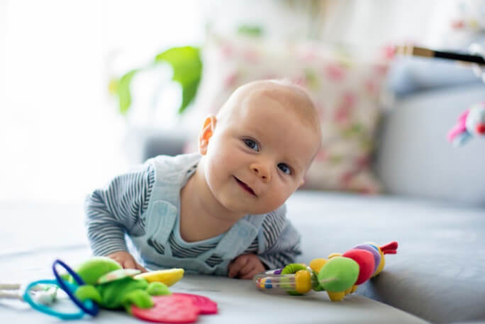 Bebé deitado num sofá com alguns brinquedos. Exercícios de estimulação precoce para o desenvolvimento do bebé.