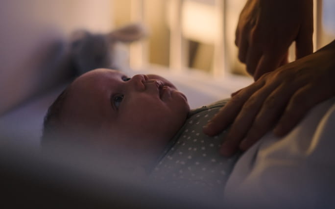   Mãos de uma mãe que vigia o sono do bebé, que sofre de insónia infantil.