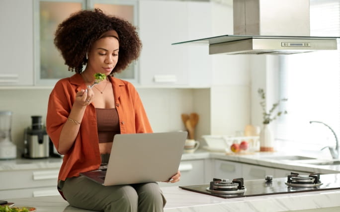 Mulher jovem, sentada na bancada da cozinha, a pesquisar sobre o que é o botulismo.