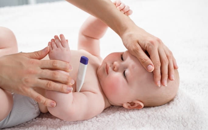 Bebé com aspeto saudável corado por causa da gripe mede temperatura com termómetro na axila.
