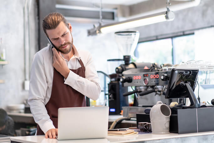 Jovem gere o novo negócio de café com telemóvel e portátil à mão 