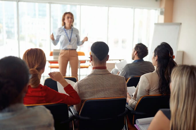 Mulher em pé a dar formação a trabalhadores.