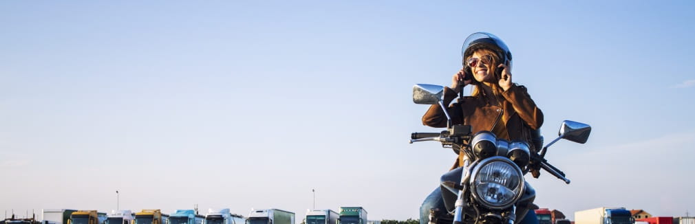 Jovem mulher sorridente a andar de moto numa rua da cidade.