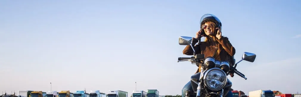 Jovem mulher sorridente a andar de moto numa rua da cidade.