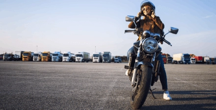 Jovem mulher sorridente a andar de moto numa rua da cidade.
