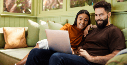 Casal sorridente sentado no sofa verifica portatil Casal sorridente faz um seguro de vida online, sentado no sofá com portátil nos joelhos