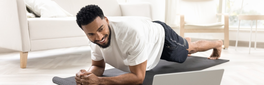 Homem jovem faz exercício em casa seguindo uma aula online.