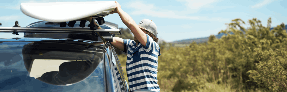 Homem jovem a colocar carga nas barras tejadilho do seu carro.
