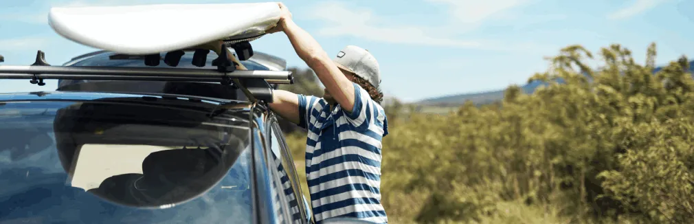 Homem jovem a colocar carga nas barras tejadilho do seu carro.