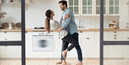 Casal jovem feliz, a dançar na cozinha, depois de ter subscrito o seguro recheio casa.